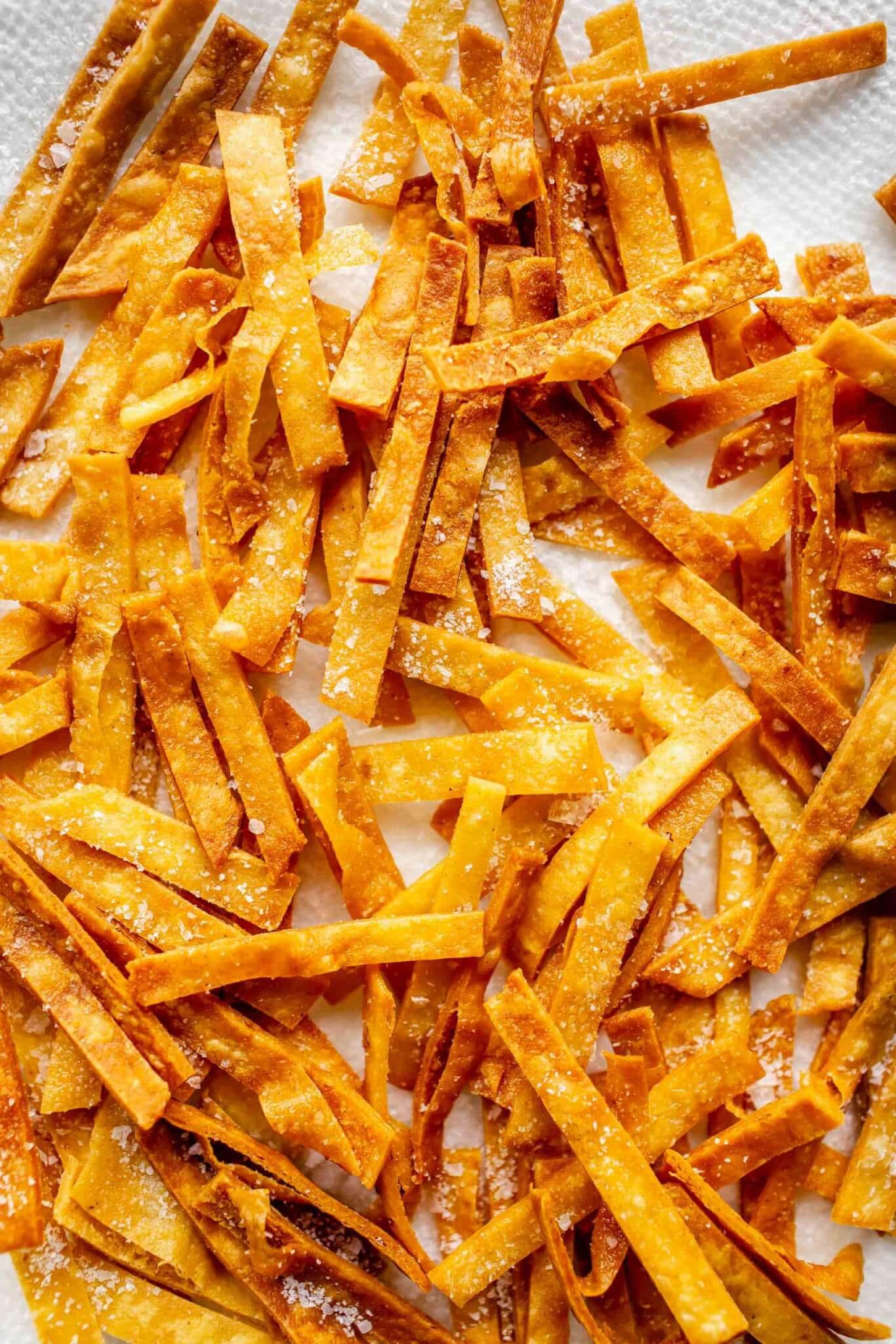 Crispy baked tortilla strips on paper towel lined tray.