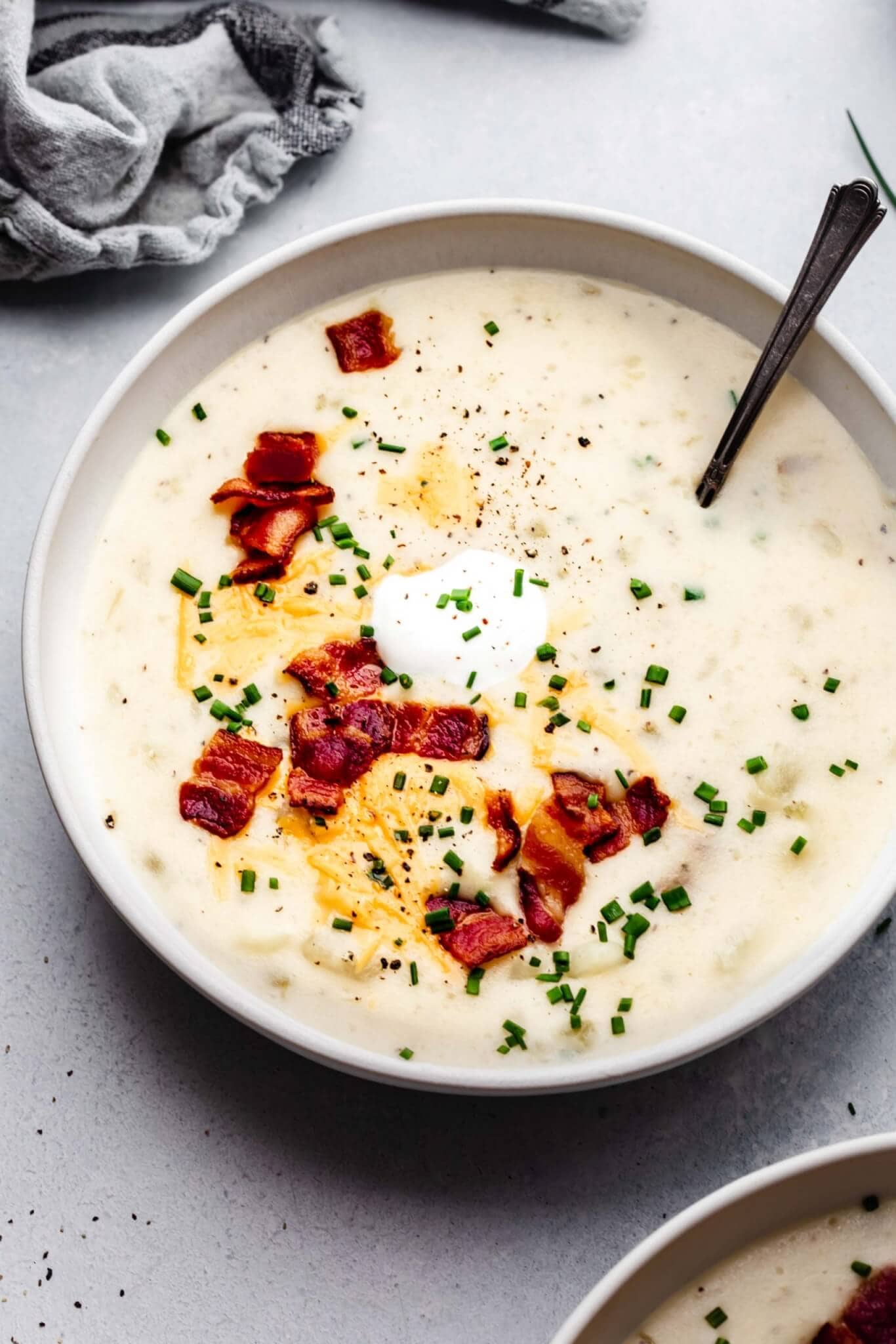 Side view of bowl of potato soup topped with cheese, bacon and sour cream.