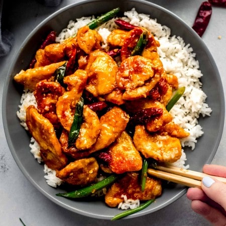 Hand holding chopsticks digging into bowl of mongolian chicken.