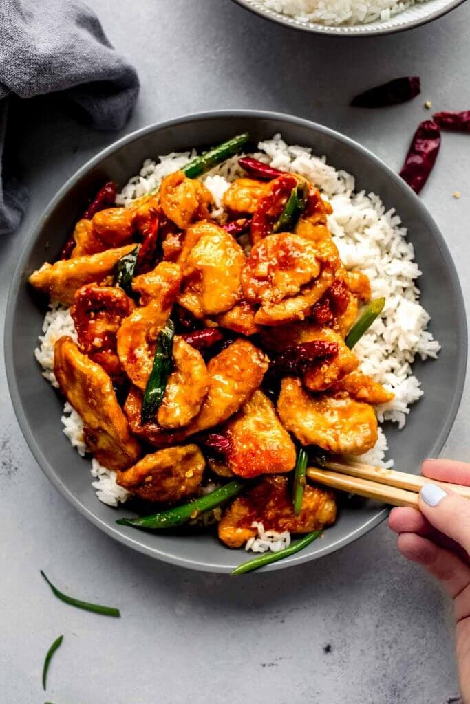 Hand holding chopsticks digging into bowl of mongolian chicken.