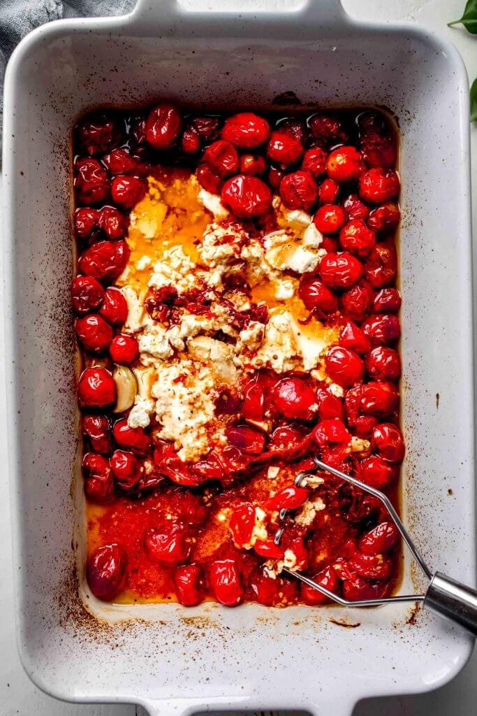 Feta and tomatoes being smashed in casserole dish.