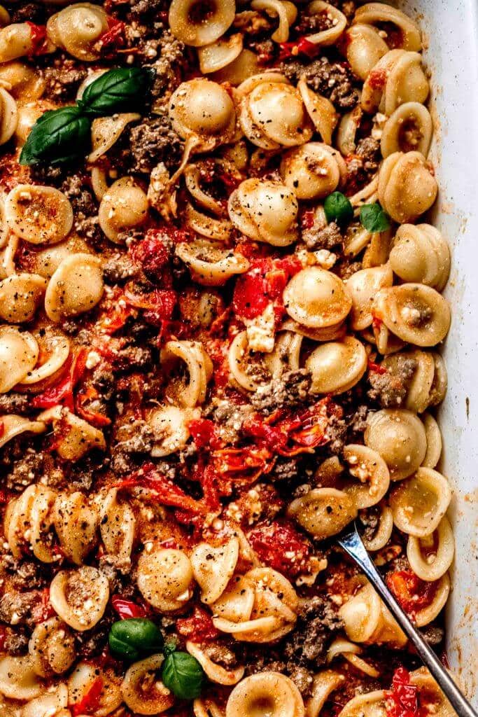 Feta and tomatoes tossed with pasta and lamb in casserole dish.
