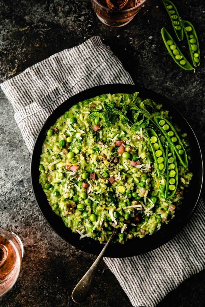 Bowl of pea risotto next to 2 glasses of rose wine.