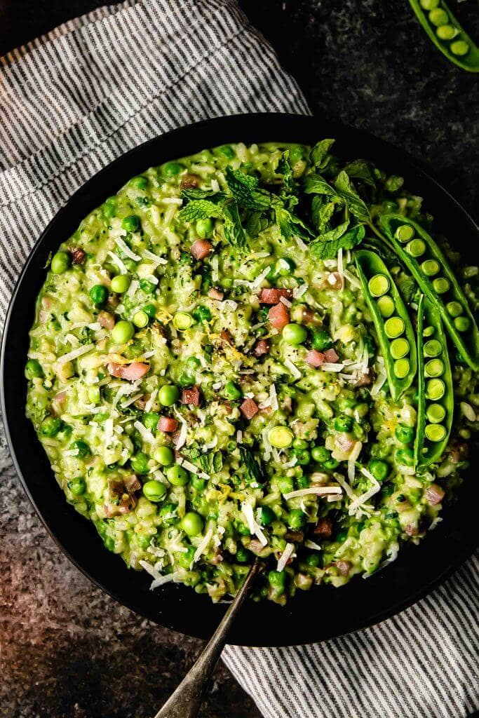 Pea risotto in black bowl with serving spoon. 