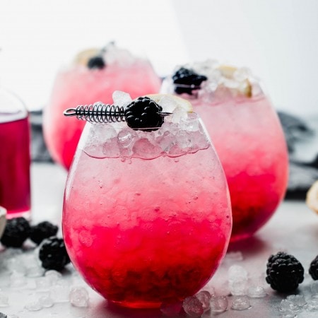Side view of bramble cocktail garnished with lemon and blackberry.