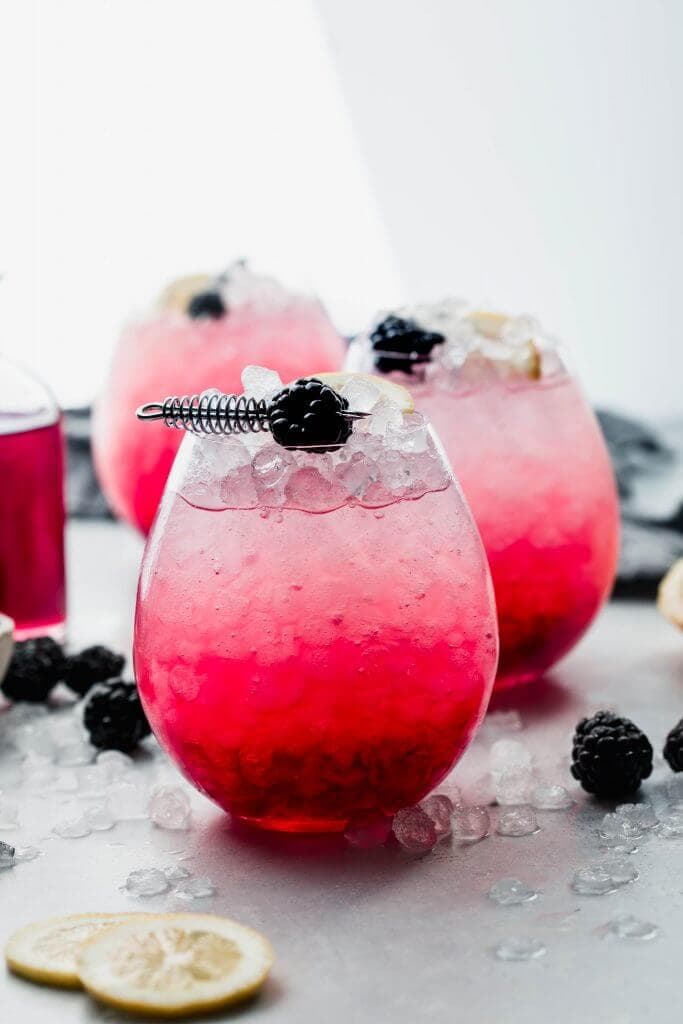 Side view of bramble cocktail garnished with lemon and blackberry.