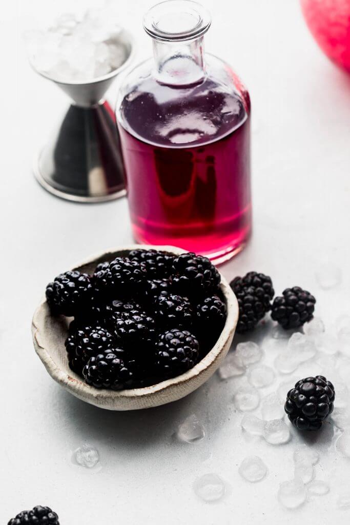 Bowl of blackberries next to blackberry simple syrup container. 
