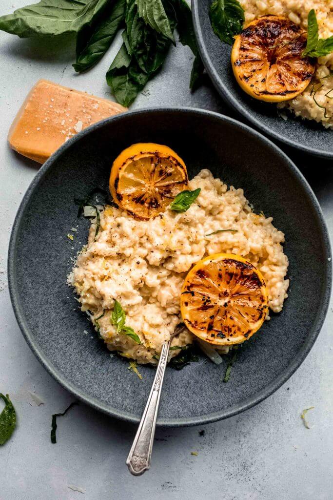 Lemon risotto in grey bowl topped with charred lemon and basil sprigs.