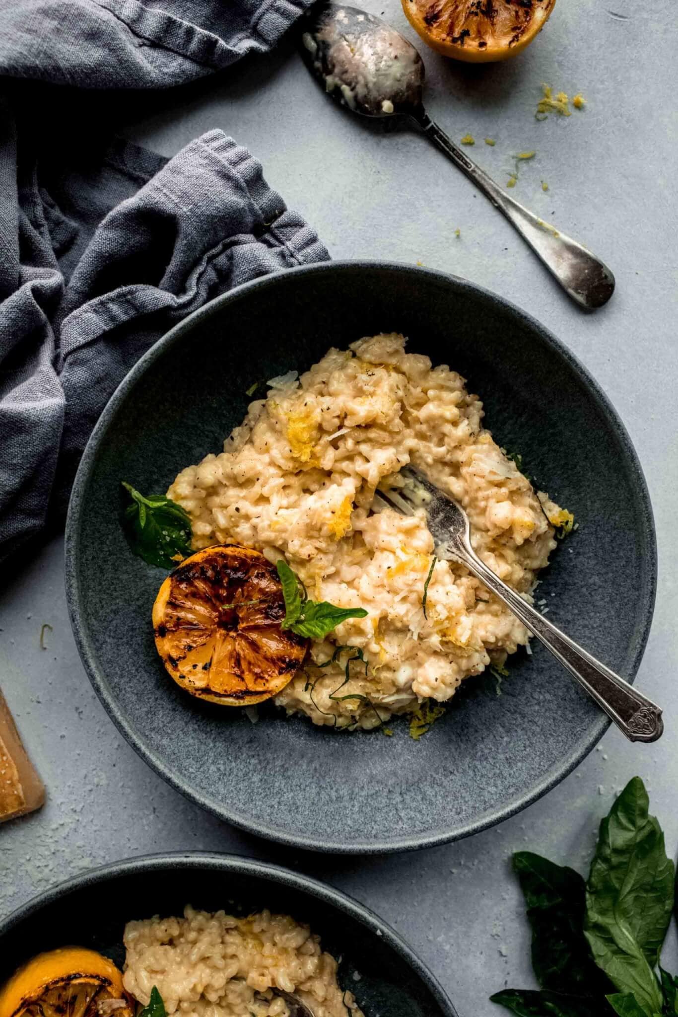 Lemon risotto in grey bowl topped with charred lemon and basil sprigs.