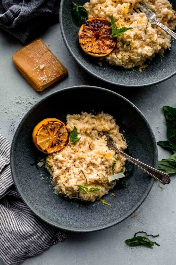 Two bowls of lemon risotto next to parmesan rind. 
