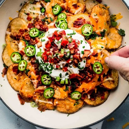 Hand reaching for irish nacho in pan.