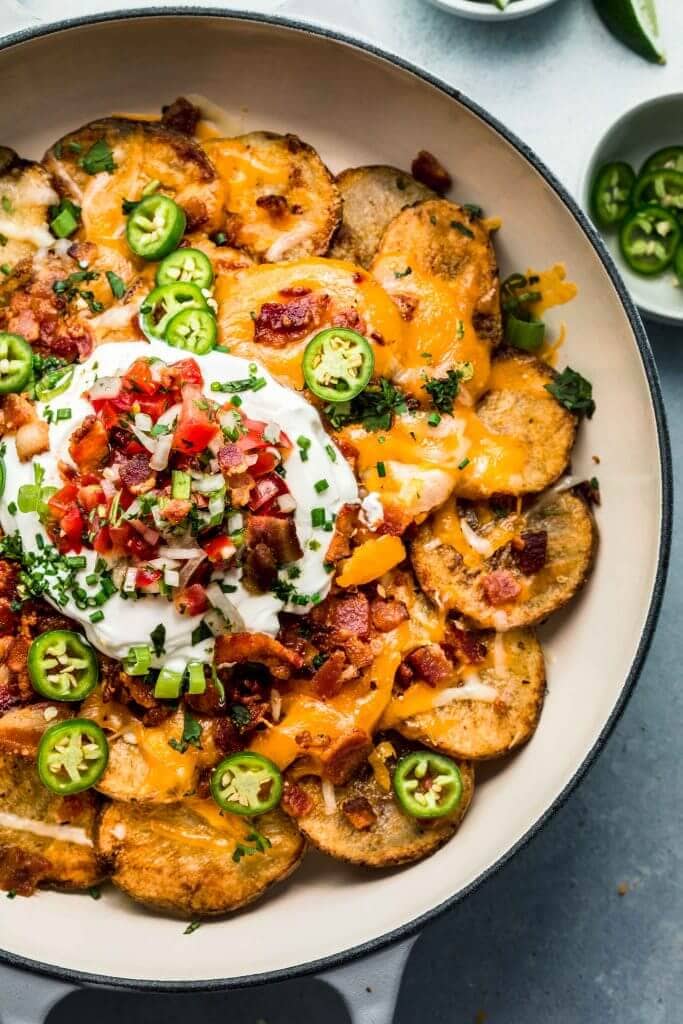 Overhead closeup of potato nachos topped with sour cream and pico de gallo. 