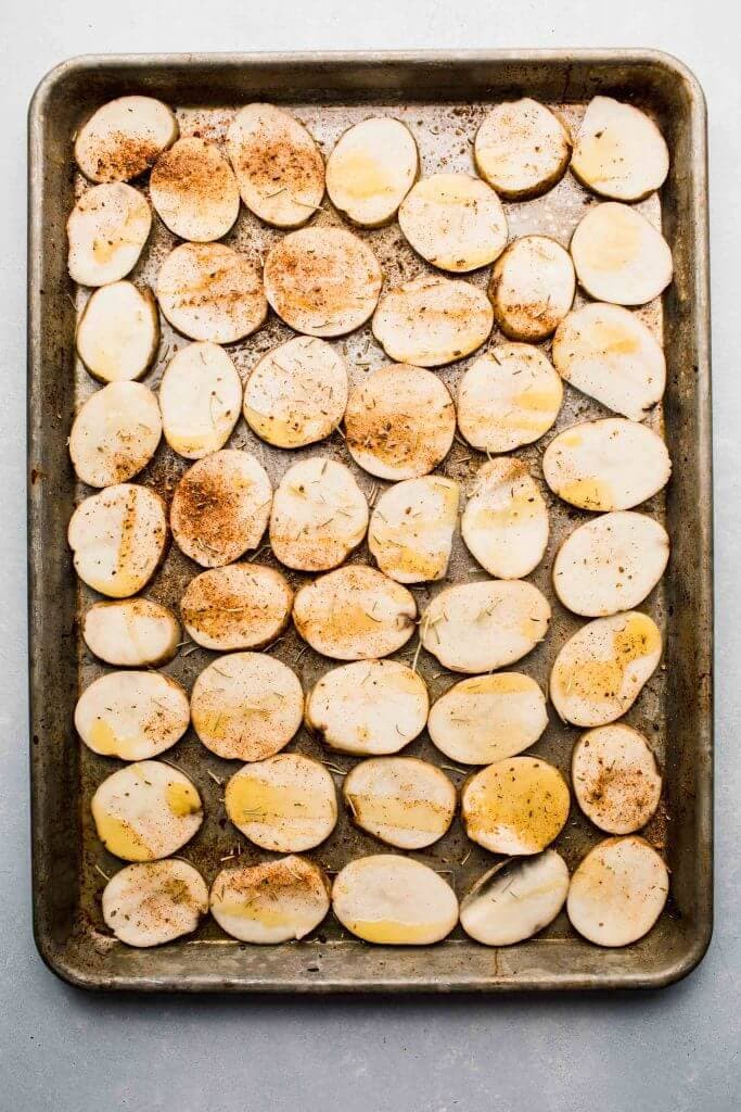 Potato slices on baking sheet sprinkled with seasonings. 