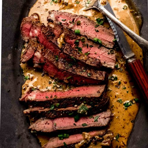 Sliced steak diane on plate with sauce.