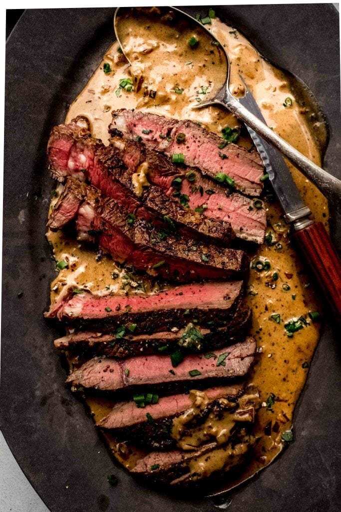 Sliced steak diane on plate with sauce.