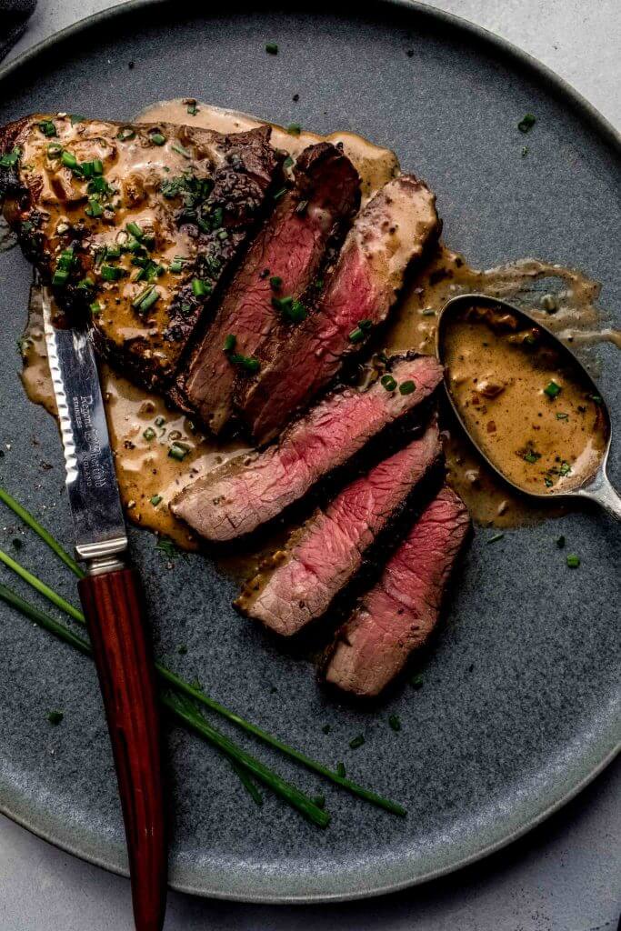 Steak sliced on plate served with diane sauce. 