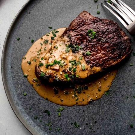Steak with diane sauce on round grey plate.