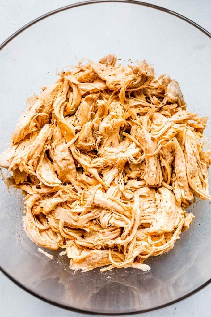 Shredded chicken in large clear glass bowl. 