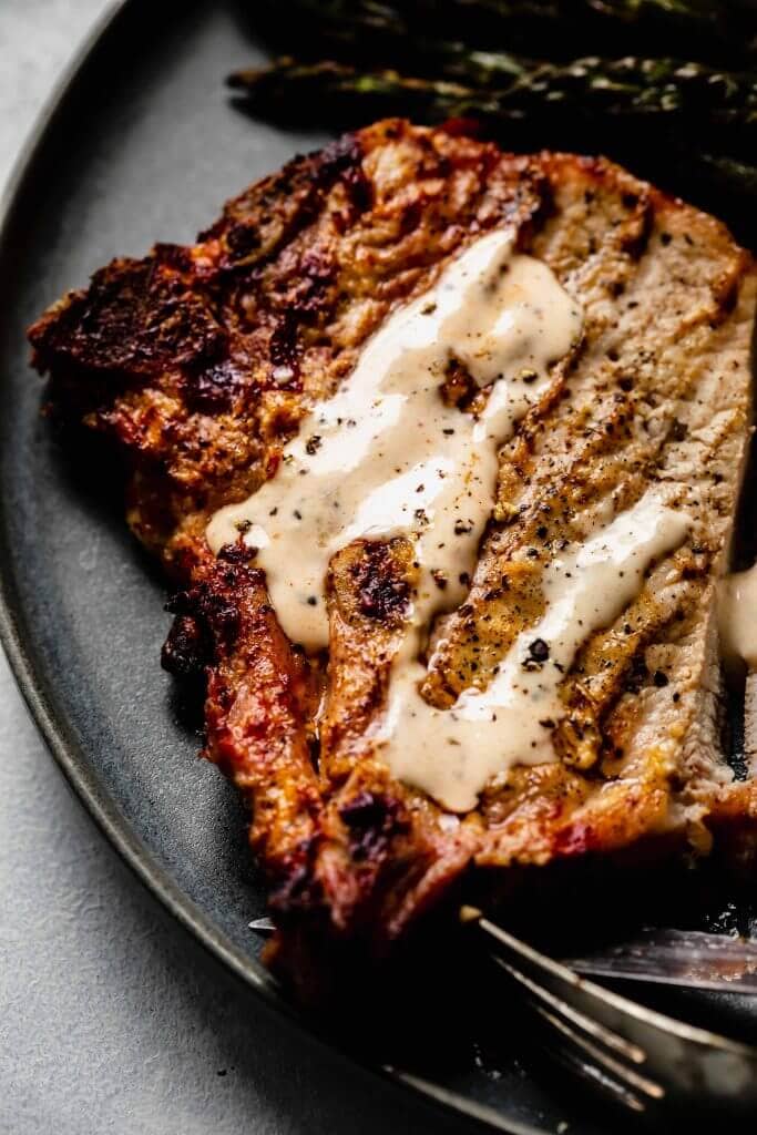 Overhead close up of pork chop topped with white bbq sauce on grey plate.