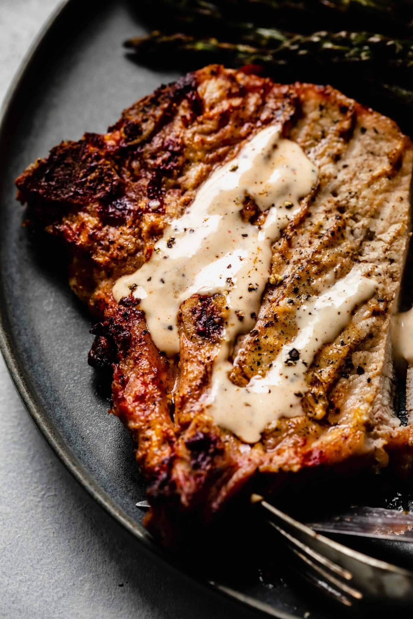 Overhead close up of pork chop topped with white bbq sauce on grey plate.