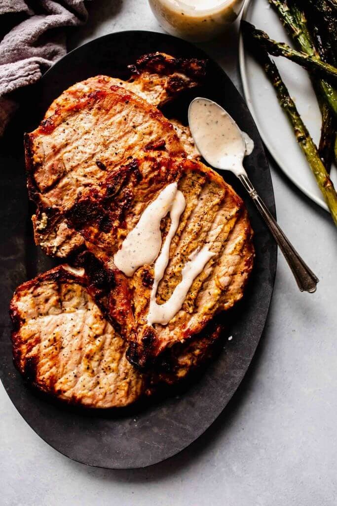 Grilled pork chops on plate drizzled with white bbq sauce. 