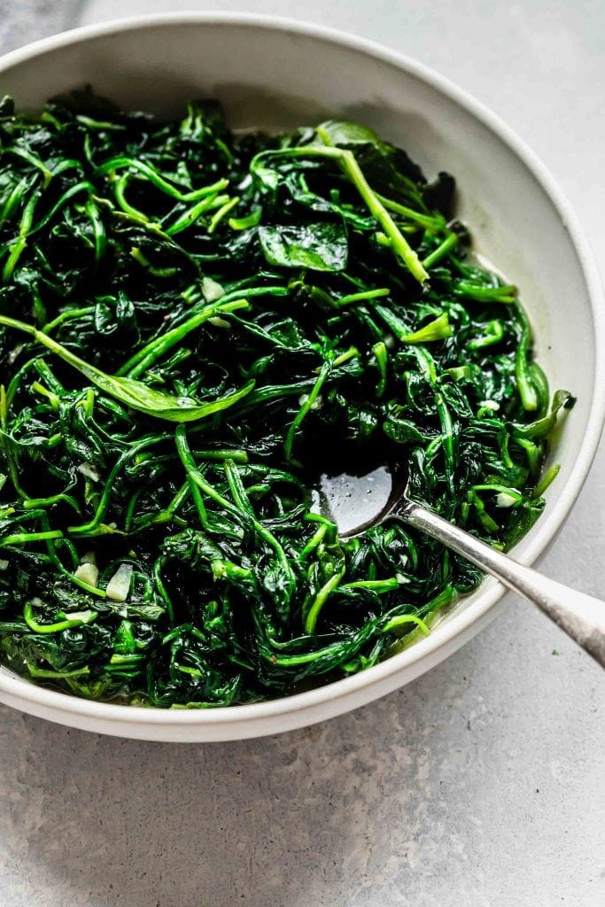 SIDE VIEW OF SAUTEED SPINACH IN WHITE BOWL. 