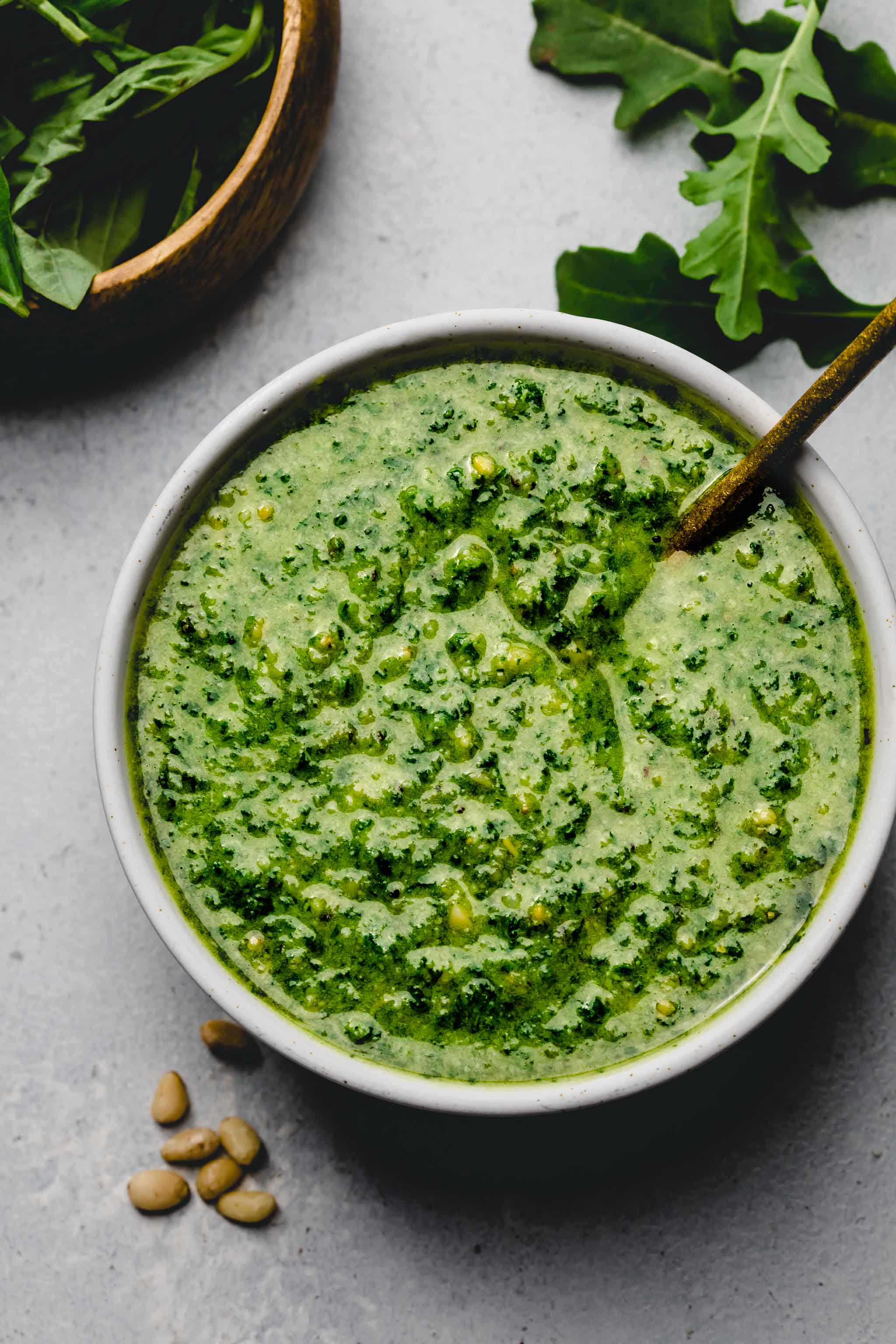 Arugula pesto in small white bowl with spoon.