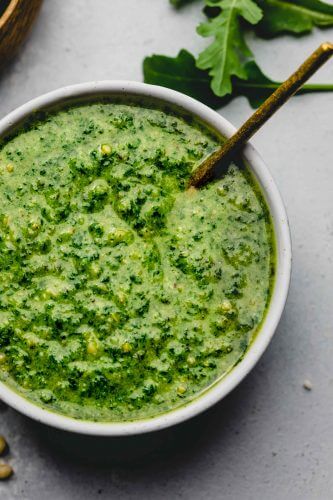Basil Arugula pesto in small white bowl with spoon.