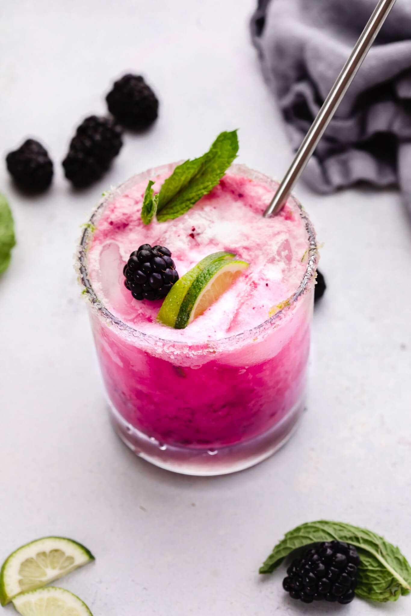 Side view of blackberry mojito on counter next to lime wedges and berries.