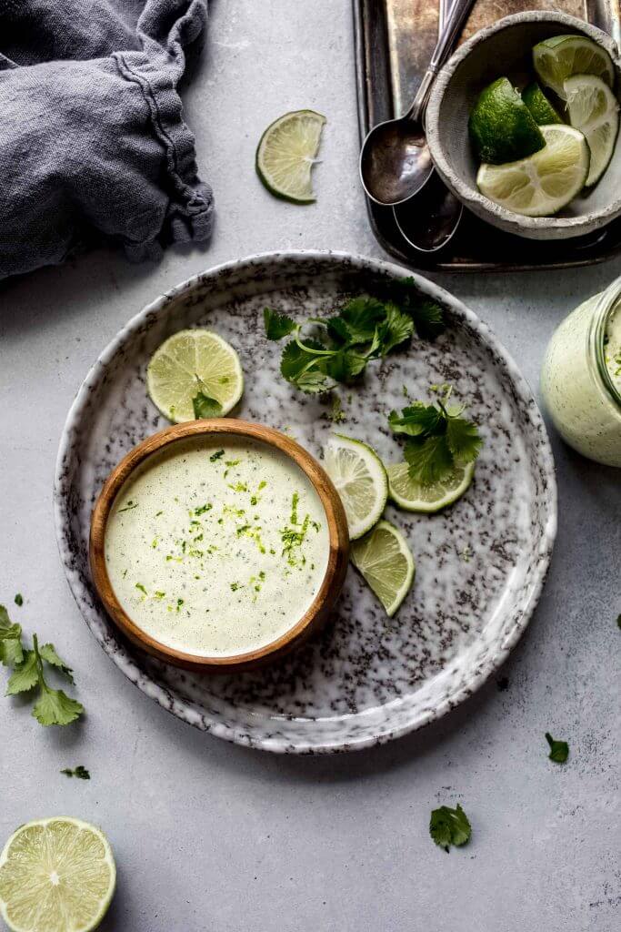 Crema in small wooden bowl on grey plate next to lime wedges. 