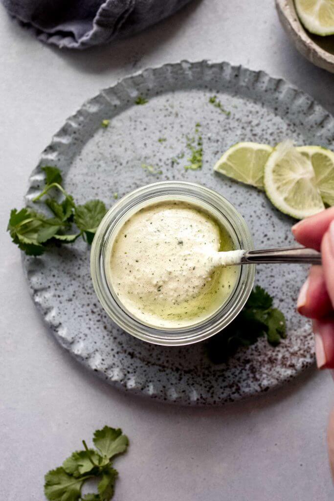 Hand dipping spoon into cilantro lime crema. 