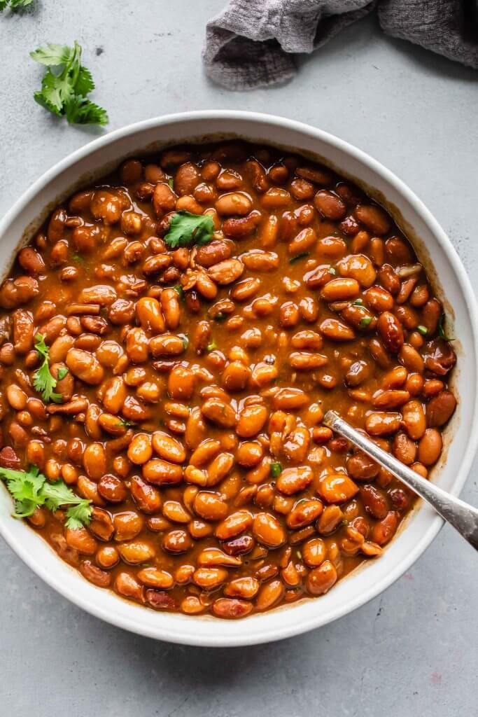 Bowl of cooked pinto beans flecked with cilantro.