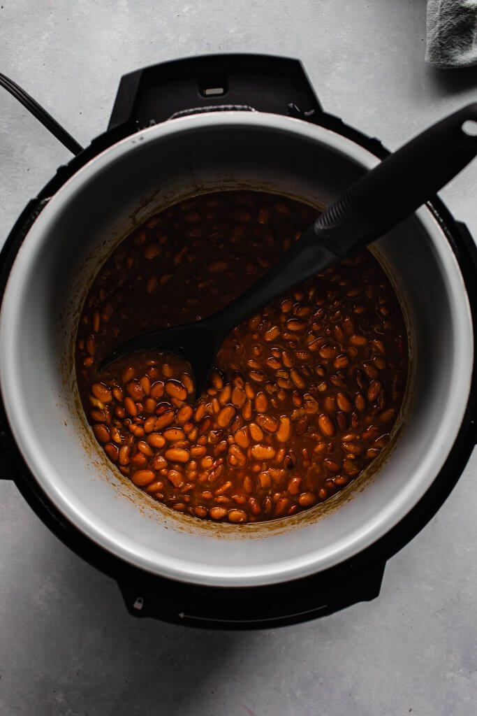 Cooked pinto beans in the instant pot with serving spoon. 