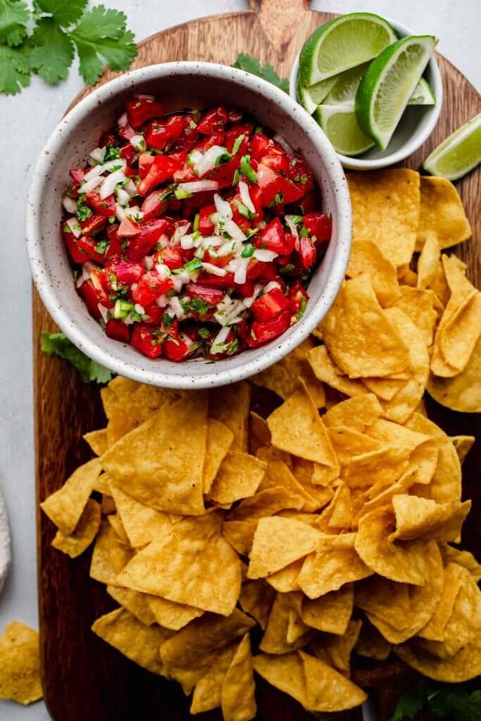 Pico de gallo on serving tray with chips and lime wedges. 