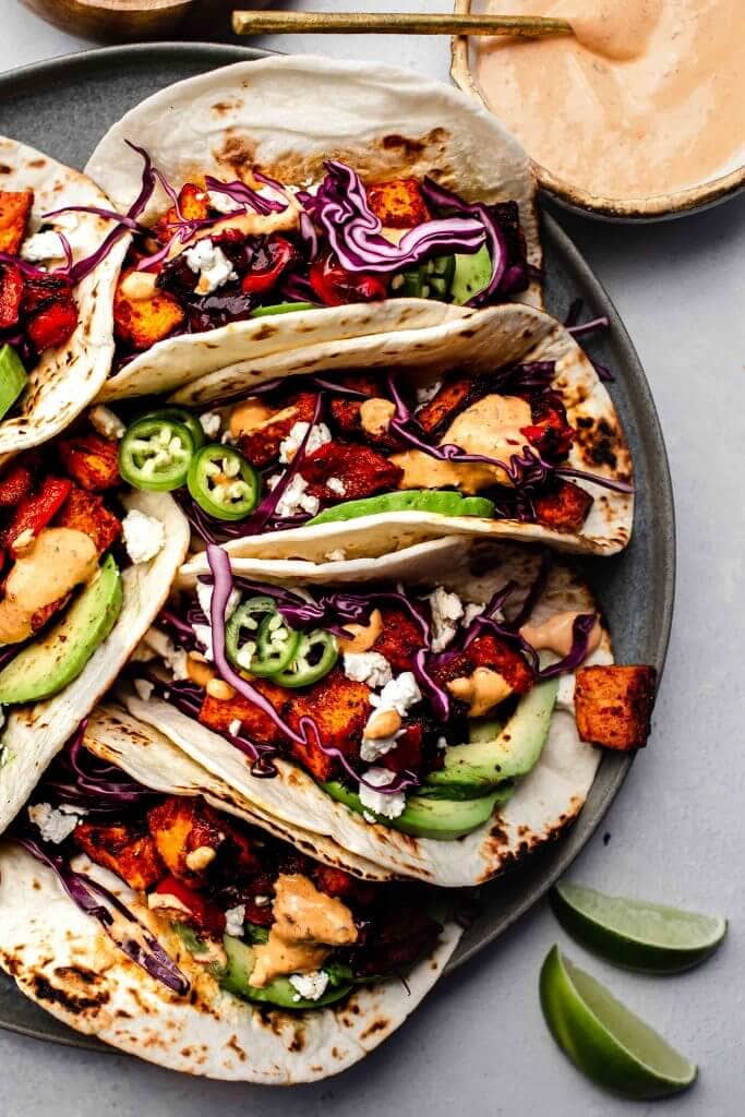 Sweet potato tacos arranged on plate next to bowl of chipotle crema. 