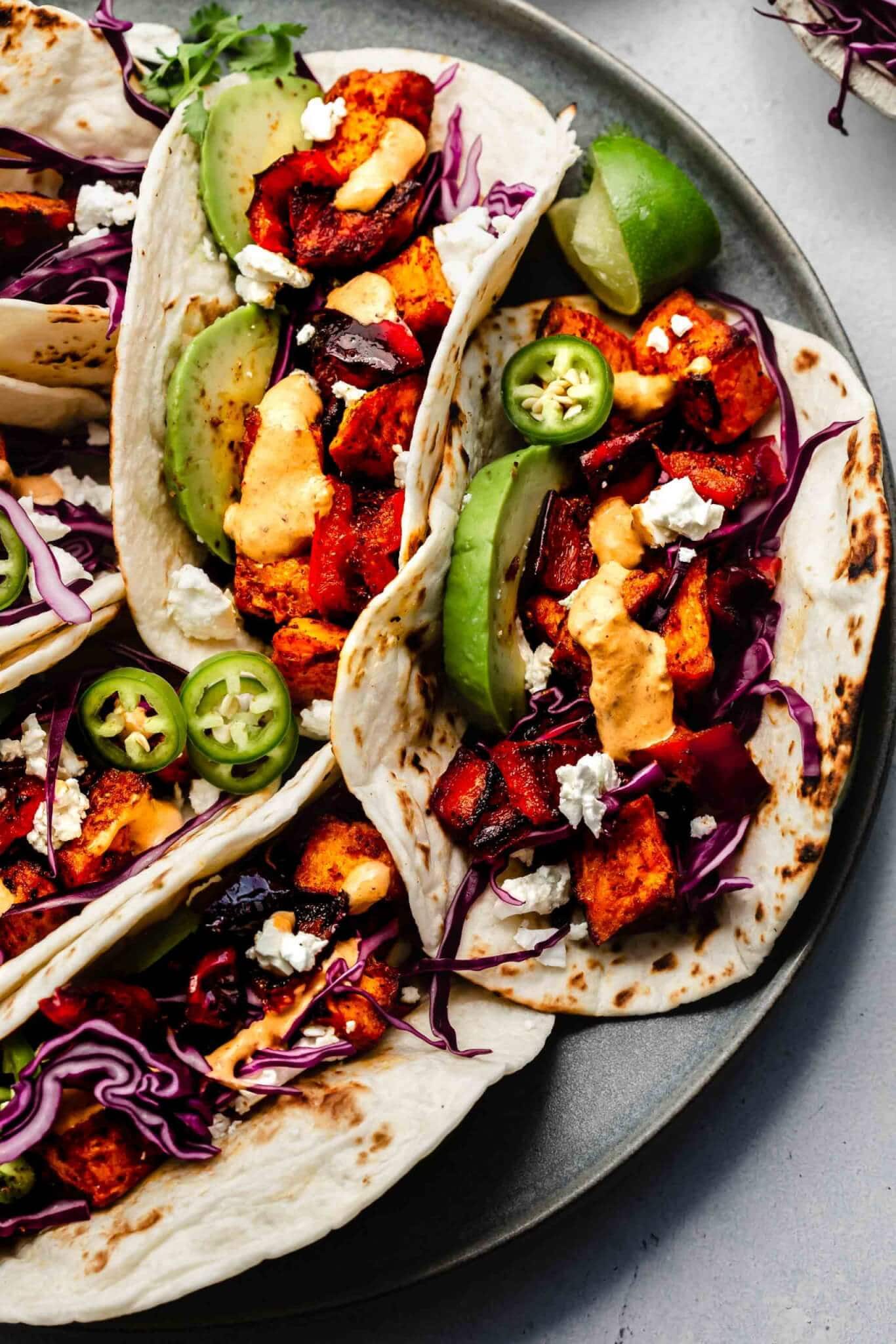 SWEET POTATO TACOS ARRANGED ON PLATE WITH TOPPINGS.