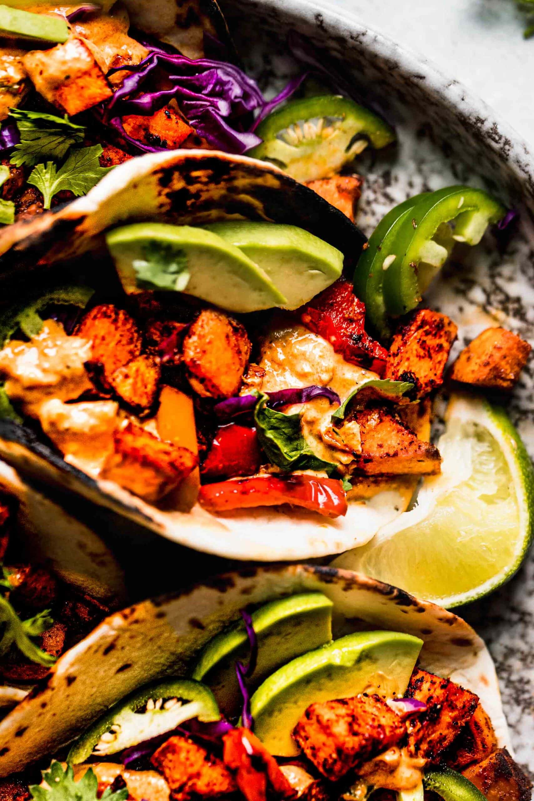 Sweet potato tacos arranged on a plate with crema and avocados.