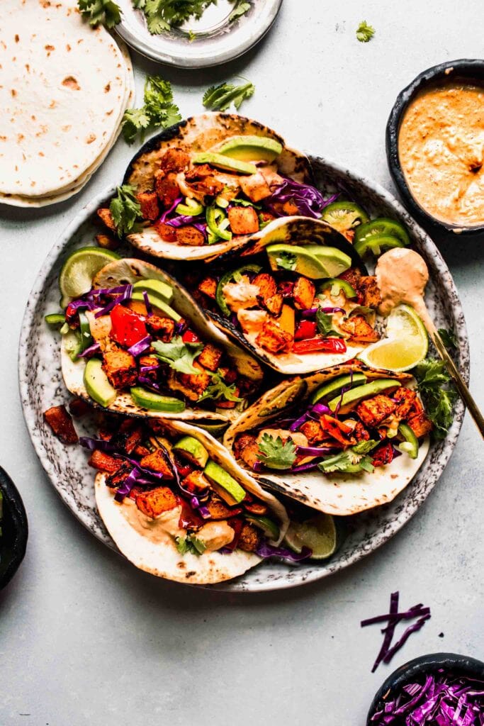 Overhead shot of sweet potato tacos arranged on plate next to small bowl of crema. 