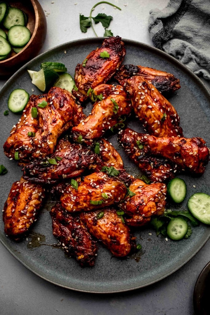 Wings arranged on grey plate scattered with cucumbers.