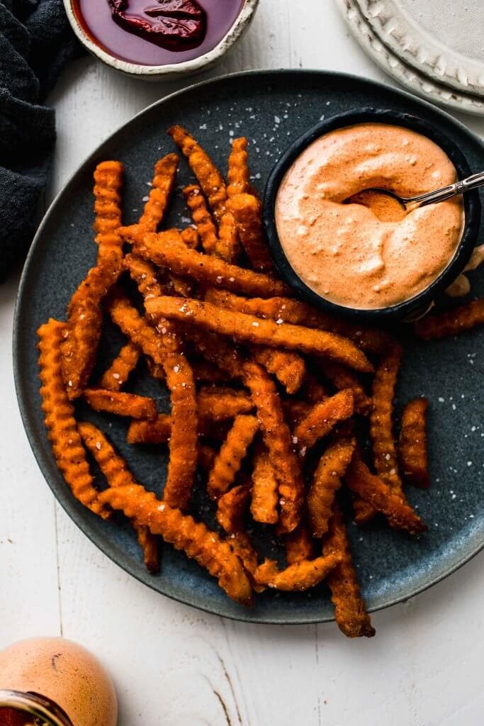 Chipotle crema in small bowl on plate of sweet potato fries. 
