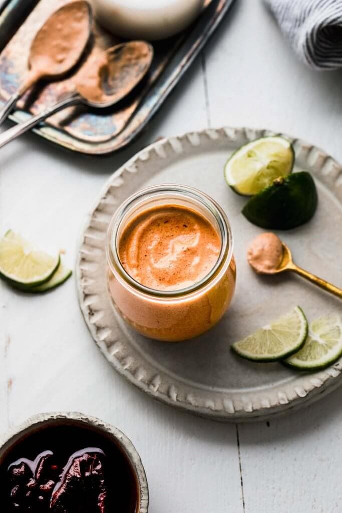 Side view of chipotle crema in jar on small plate next to bowl of chipotles. 