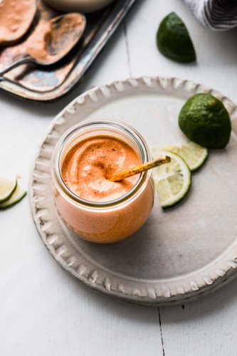Burrito sauce in glass jar next to bowl of chipotles and lime wedges.