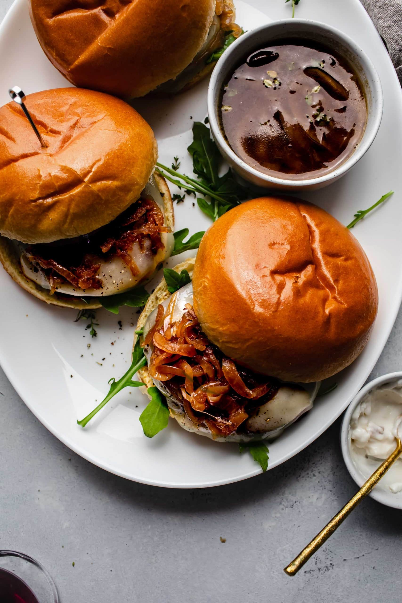 Overhead shot of french dip burgers on platter with bowl of au jus.