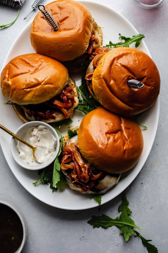 Overhead shot of french dip burgers on platter with bowl of au jus.