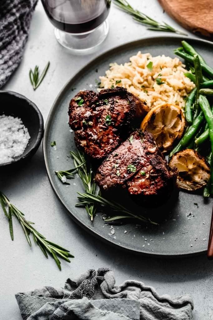 Lamb chops arranged on plate next to glass of red wine. 