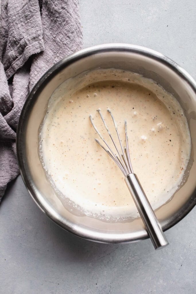 White bbq sauce in bowl with whisk.