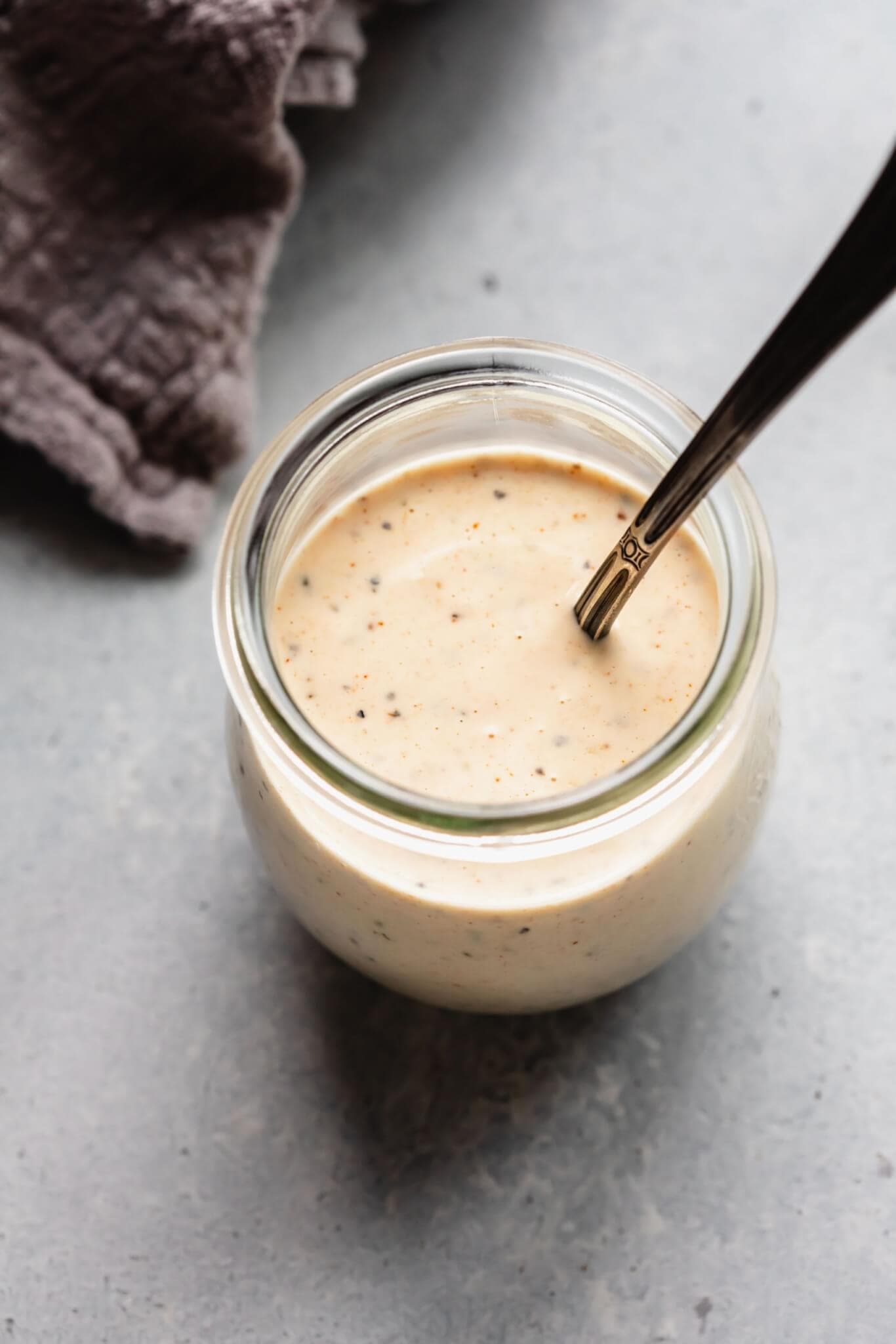 SIDE VIEW OF WHITE BBQ SAUCE IN SMALL JAR WITH SPOON.