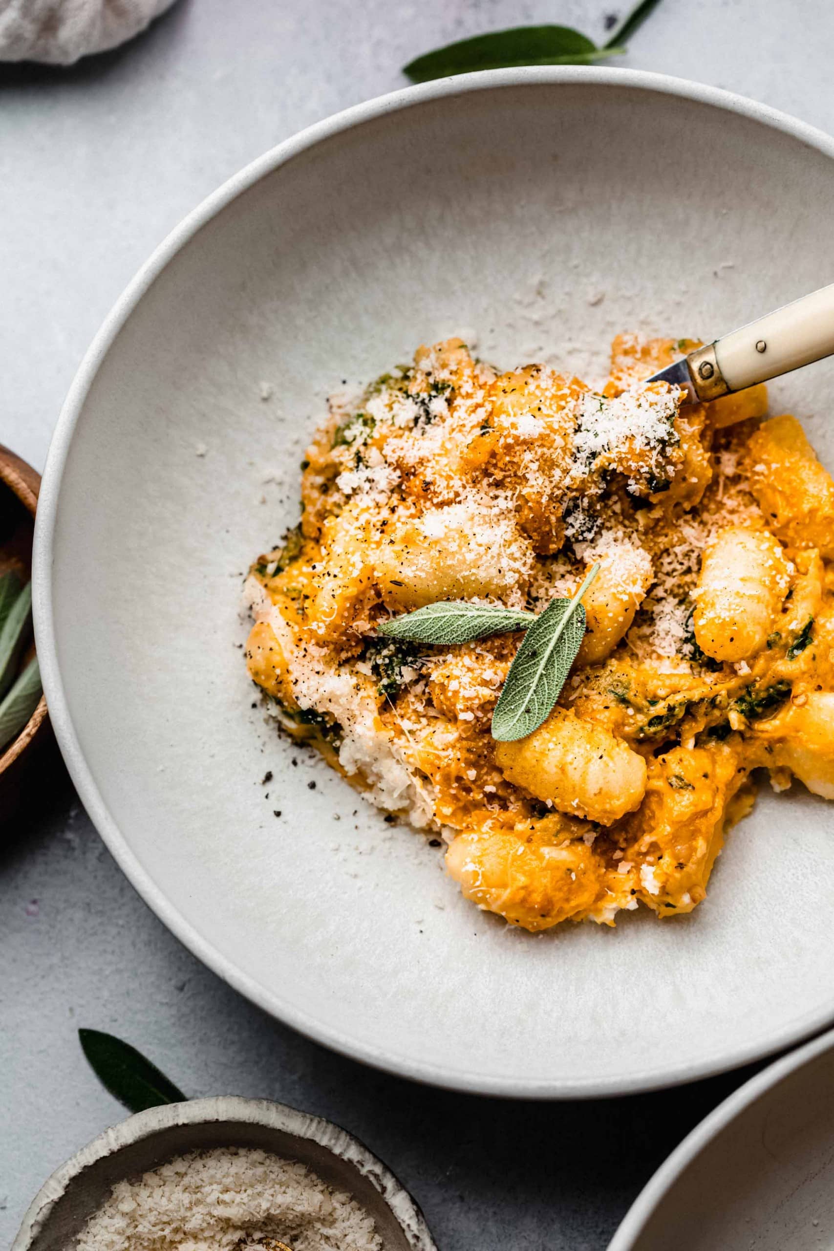 Pumpkin gnocchi in bowl topped with sage leaves.
