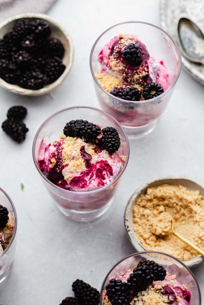 Three dishes of blackberry fool next to small bowl of cookie crumbs. 