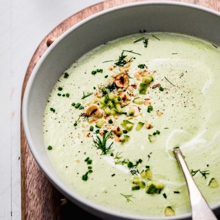 Side view of bowl of chilled cucumber soup with spoon and topped with hazelnuts.